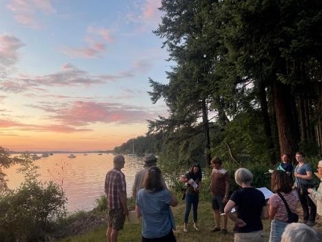 Group of people looking for bats near a waterbody as the sun sets in the background.