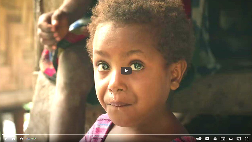 A YouTube video screenshot shows a young child with curly hair and bright eyes looks toward the camera, wearing a striped shirt. With a hint of curiosity, the child stands outdoors near a blurred backdrop.