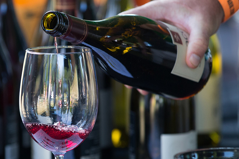 一只手从瓶中倒红酒到透明酒杯中。模糊背景中还能看到几瓶其他酒瓶。